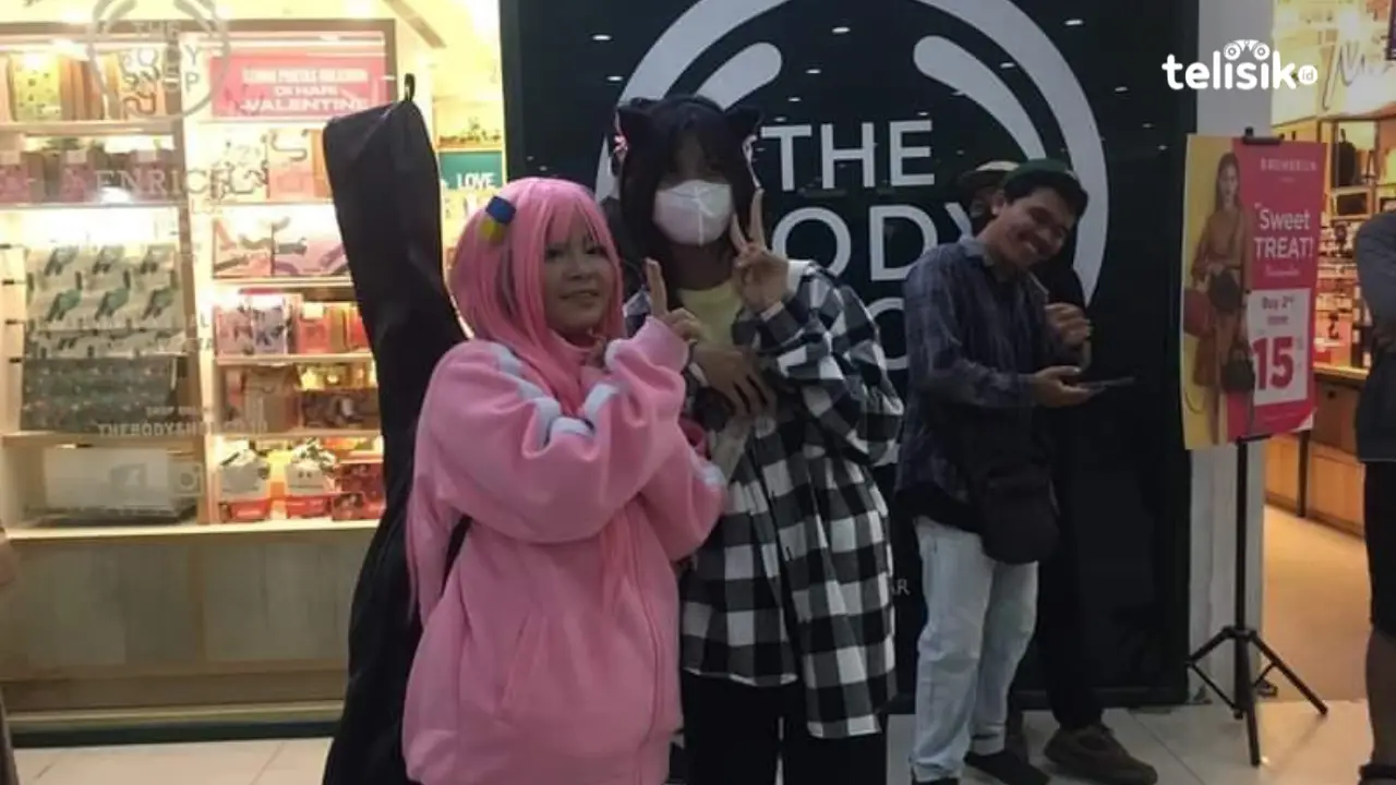 Cosplayer yang menirukan karakter Bocchi dari Animasi Bocchi The Rock, berfoto dengan pengunjung lengkap dengan atribut bawaan karakternya berupa gitar. Foto: Ahmad Badaruddin/Telisik