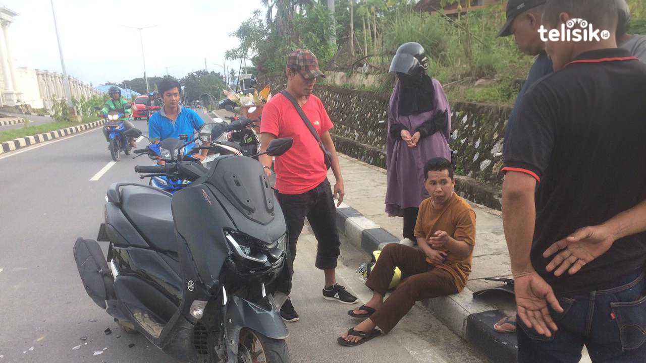Tampak sepeda motor matik mengalami pecah pada lampu depan, dan pengendara motor duduk di trotoar. Foto: Bambang Sutrisno/Telisik