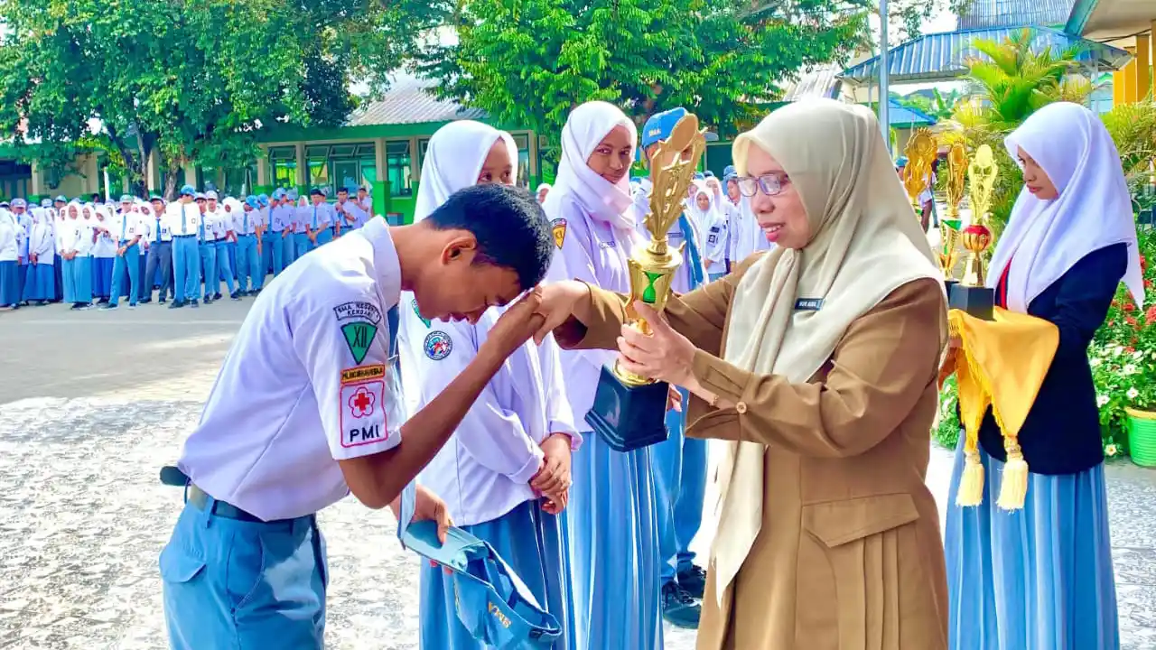 Kepsek SMAN 2 Kendari, Nur Aida, saat menyerahkan seragam gratis sekaligus memanggil siswa berprestasi saat upacara. Foto: Ist.