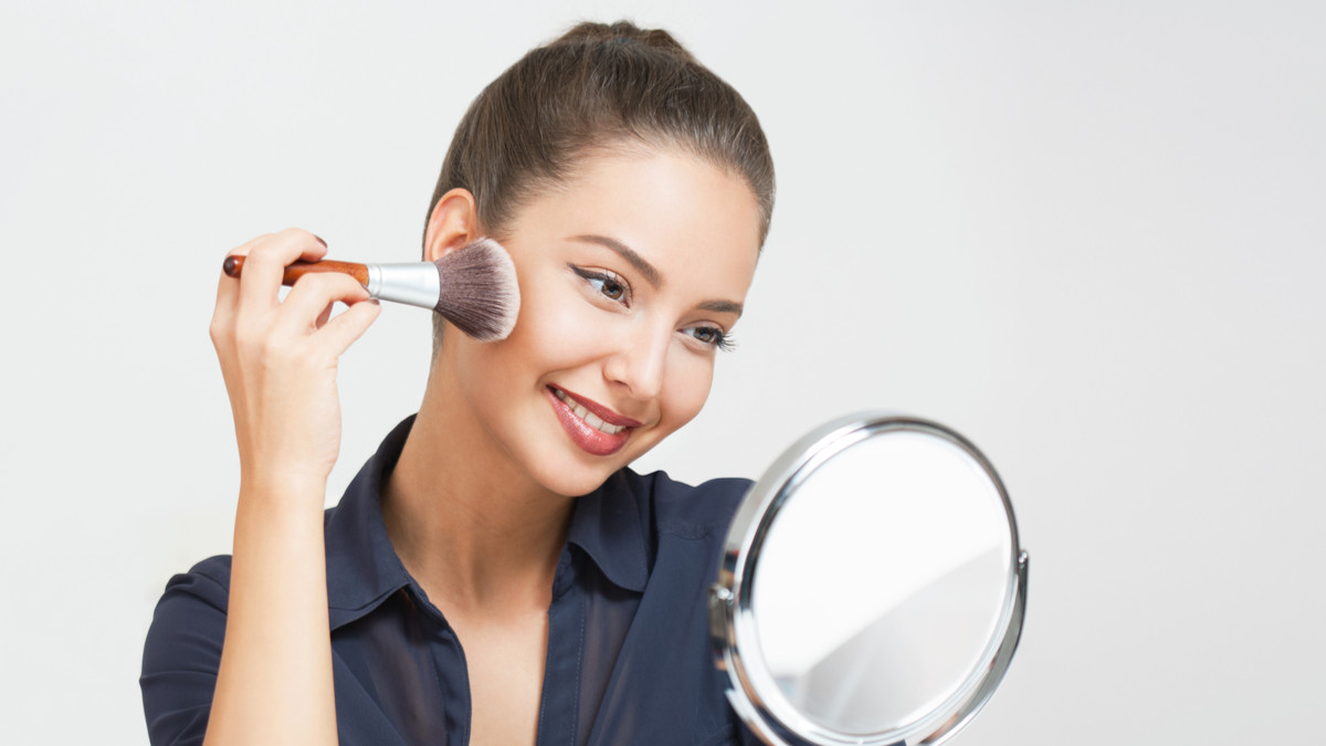 Ilustrasi seorang perempuan sedang mengaplikasikan foundation pada wajah menggunakan kuas makeup untuk membantu meratakan warna kulit dan menyamarkan noda hitam. Foto: KlikDokter.com